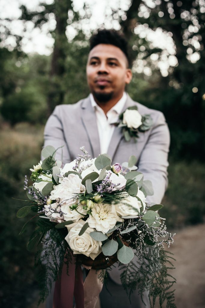 groom in grey suit holding a bouquet of white flowers