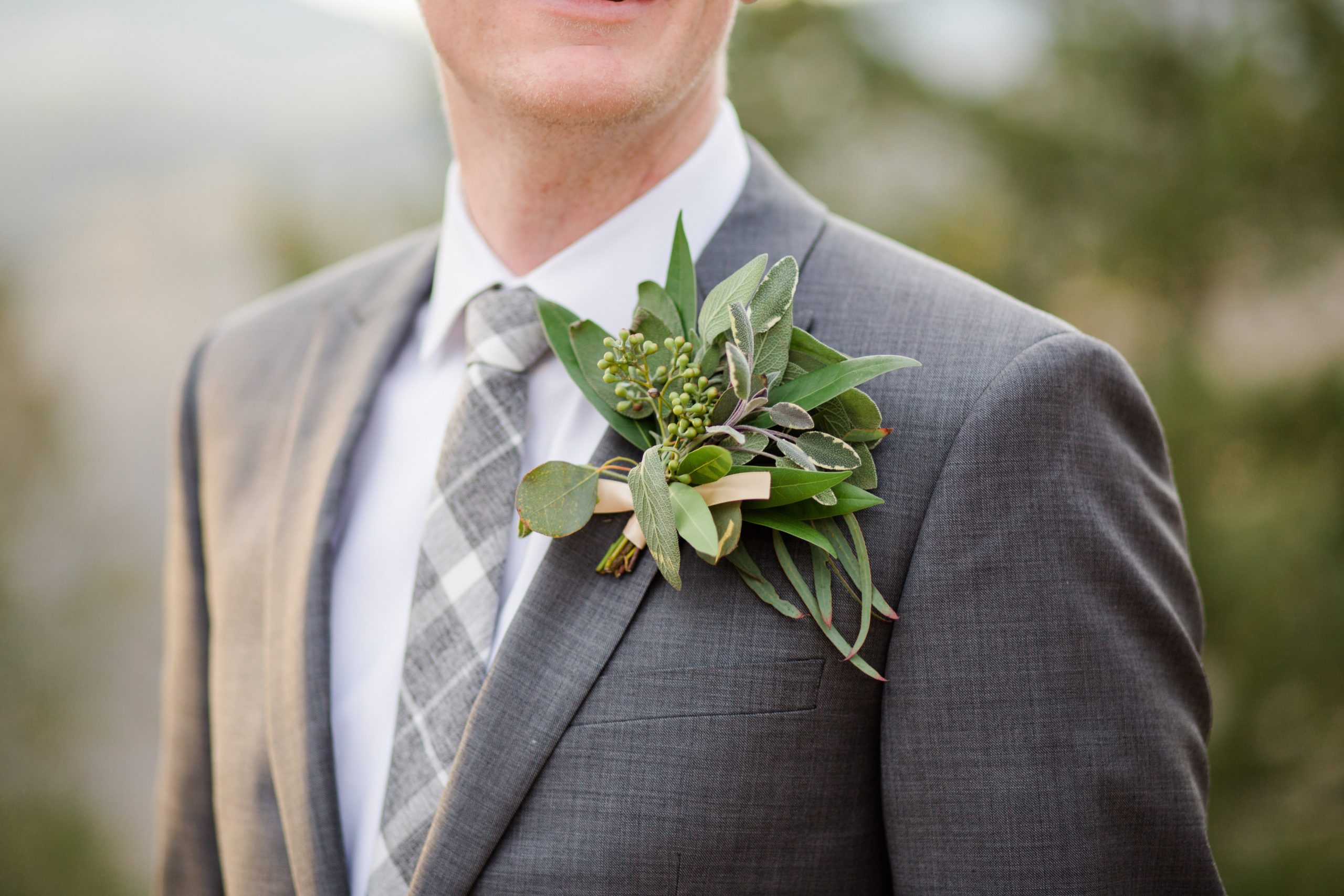 groom in grey suit with large greenery boutonnière