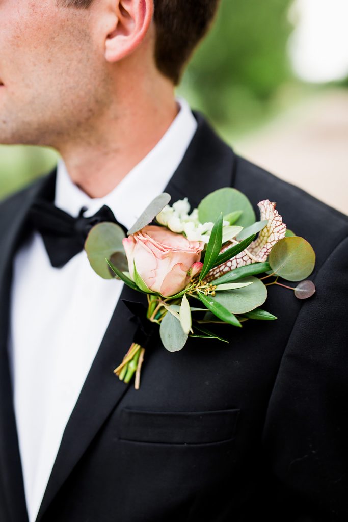 groom in a black suit with a boutonniere of eucalyptus and pink rose