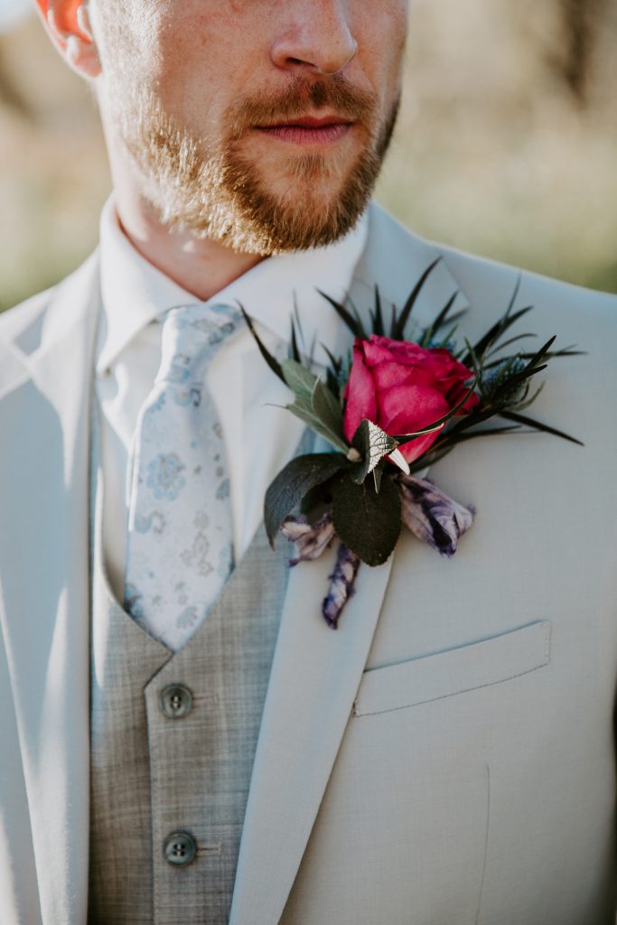 groom in a light grey suit with vest with a magenta rose boutonniere
