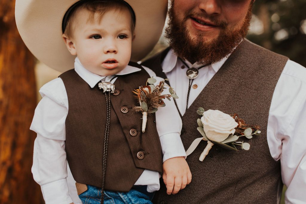 groom in brown vest holding ring bearer in cowboy hat