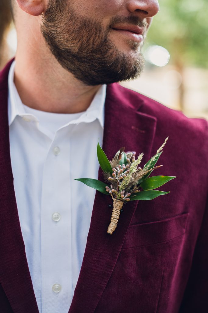 groom wearing maroon velvet jacket with boutonniere of feathers and greenery