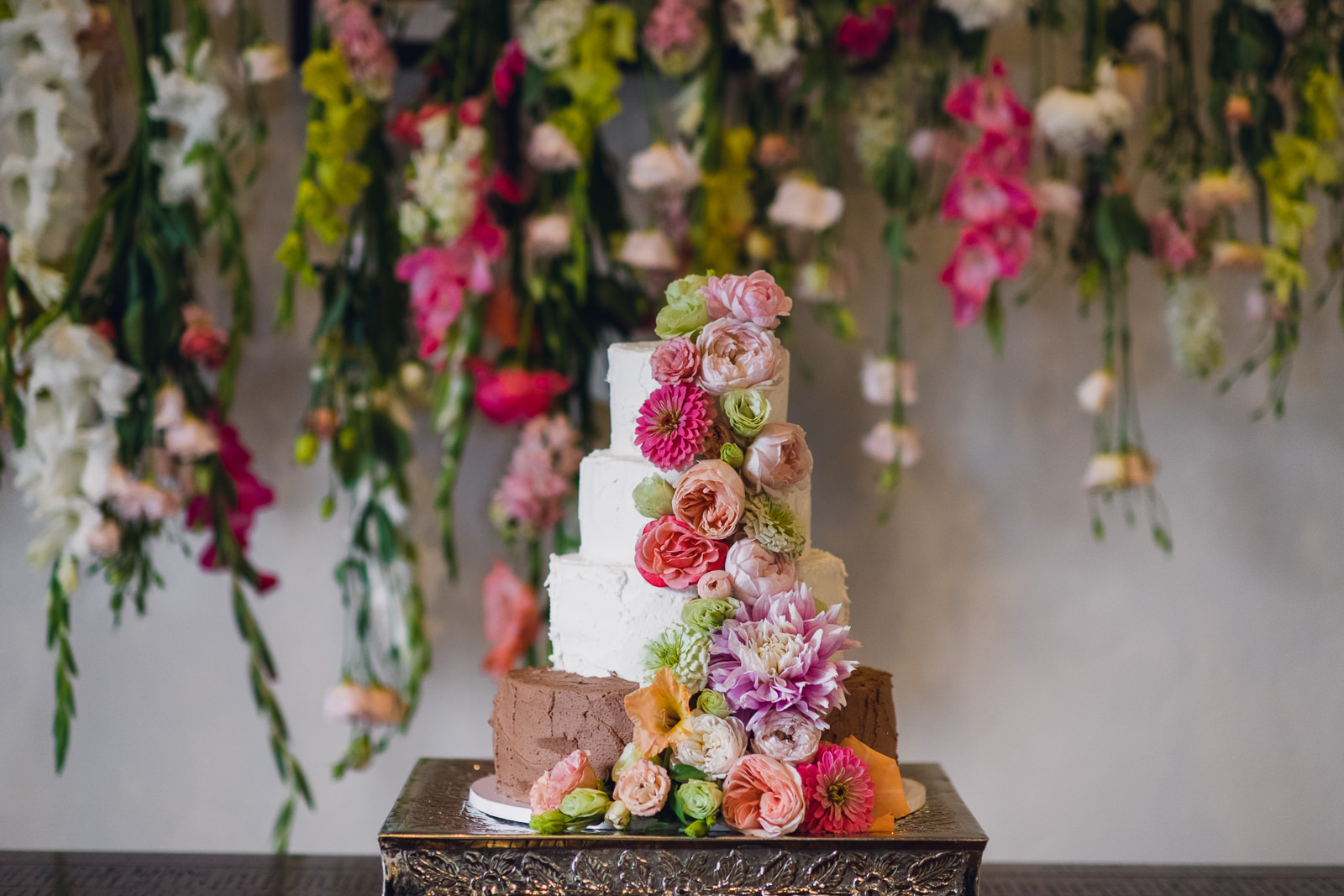 lush citrus flowers decorating wedding cake in front of a dripping floral backdrop