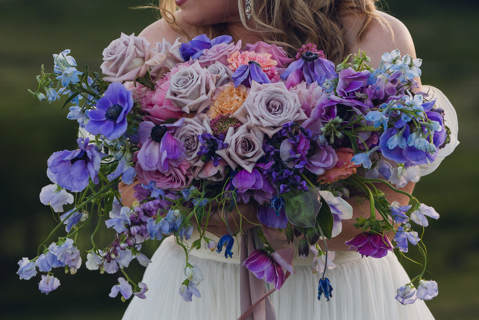 bride holding bouquet of purple anemones, roses, delphinium, sweet pea