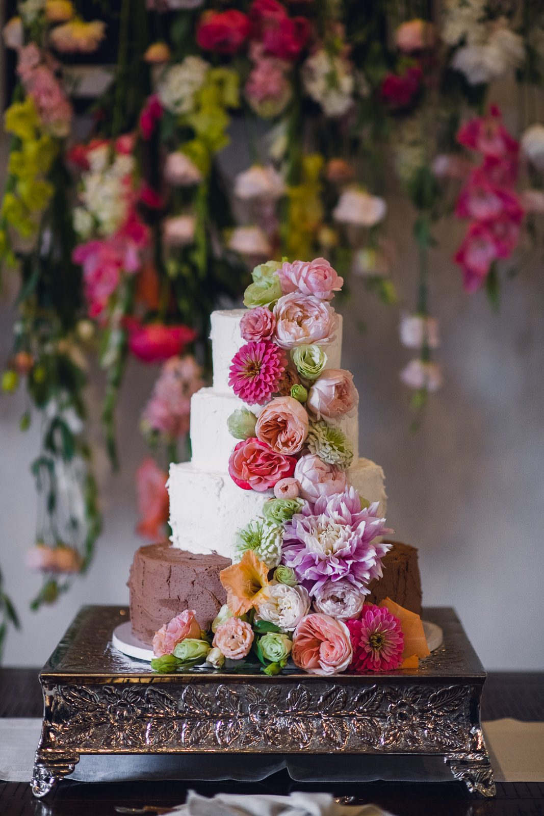 wedding cake with cascading flowers in front of a matching floral backdrop