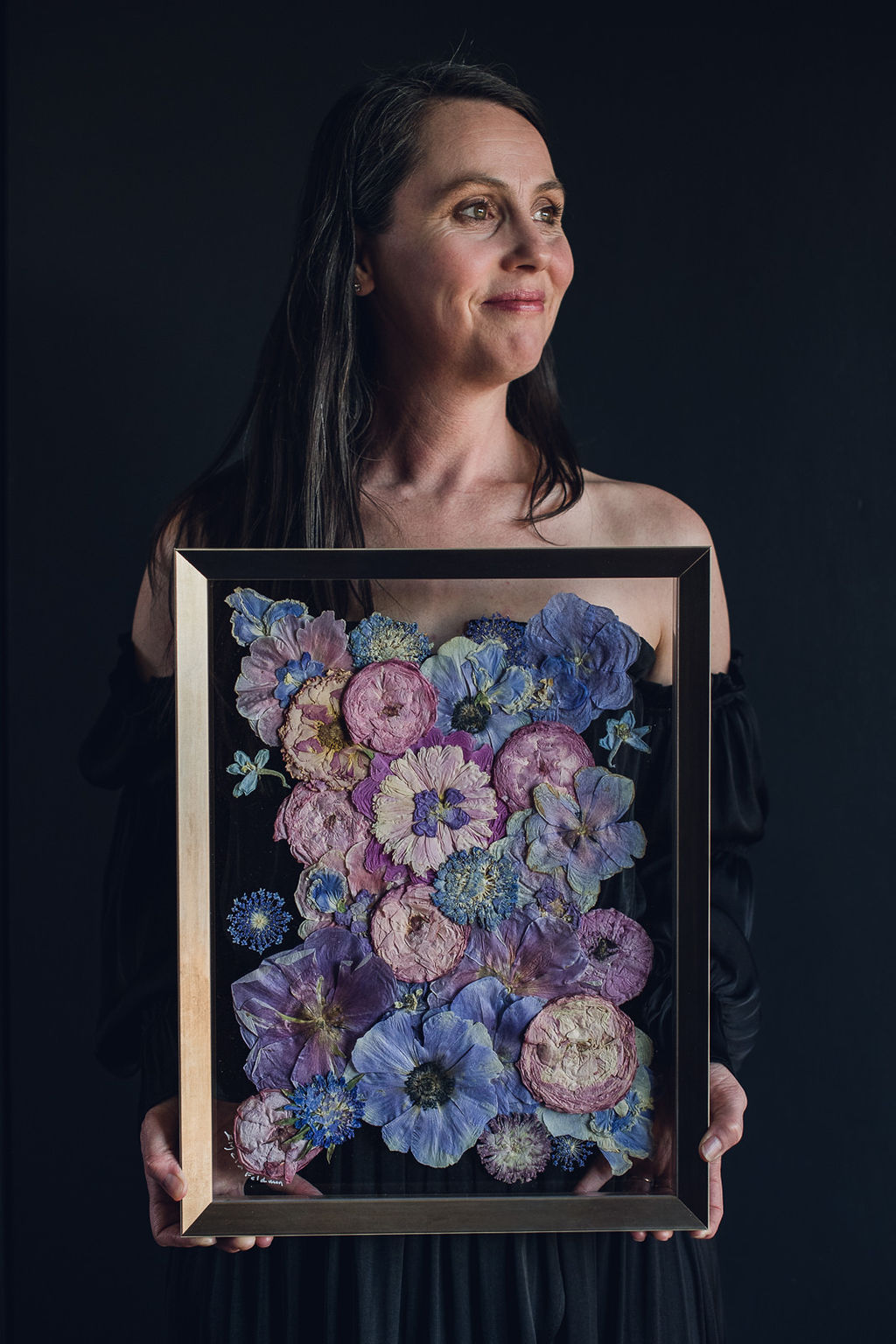 Designer Elycia Feldman holding a framed piece of pressed flower art.