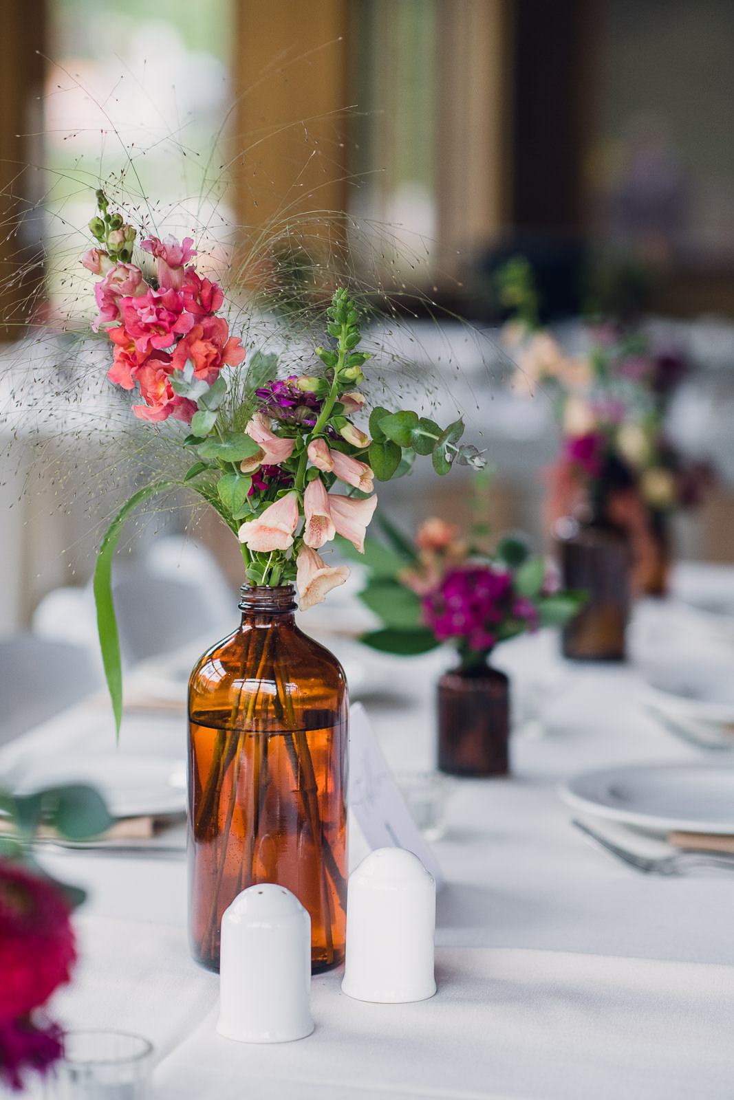 amber glass bud vases filled with shades of pink flowers lining the center of a wedding reception table