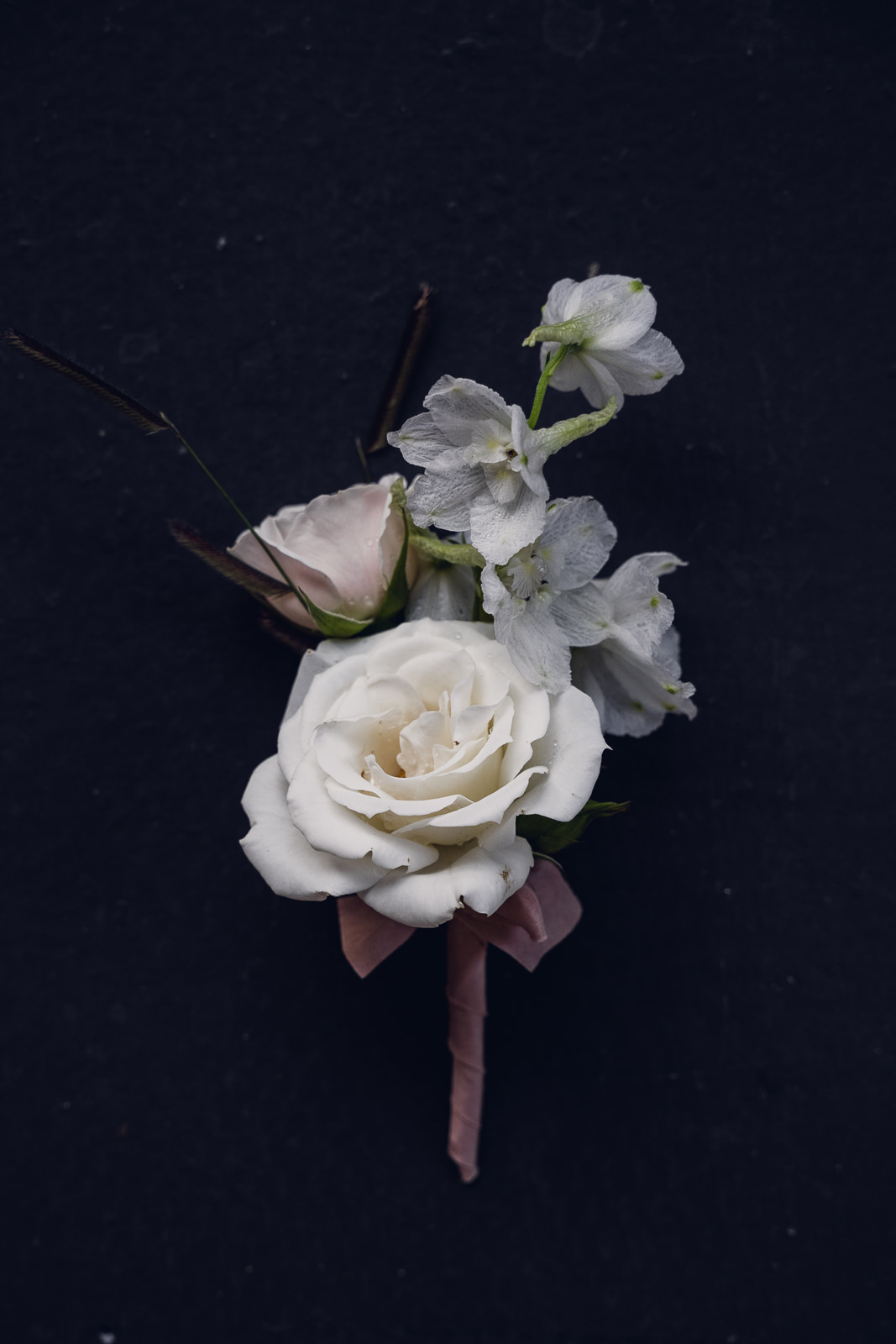 delicate white boutonniere made from rose and delphinium tied with mauve silk